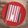 A striped 2027 diary with red and white vertical stripes and a light blue pen, arranged on a round red tray over a light wood surface.