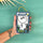 A hand holds a packaged Moomin Handwarmer. The product is wrapped in a white paper sleeve with a cartoon illustration of Moomin characters and set in a blue-gray card sleeve with a gold hanging string.