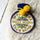 A novelty hot water bottle design of The Beatles, featuring the text 'St. Peppers Lonely Hearts Club Band' in yellow and red on a white background, with a navy blue top and yellow pom-pom ties, isolated on a white background.