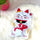 A white hot water bottle featuring an embroidered Japanese Maneki-neko (lucky cat) design with a red fish, resting on a white faux fur rug.
