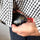 A close-up of a person holding a black fish-shaped soy sauce hand warmer with gold line art and a red cap, partially pulled from a black-and-white checkered shirt.